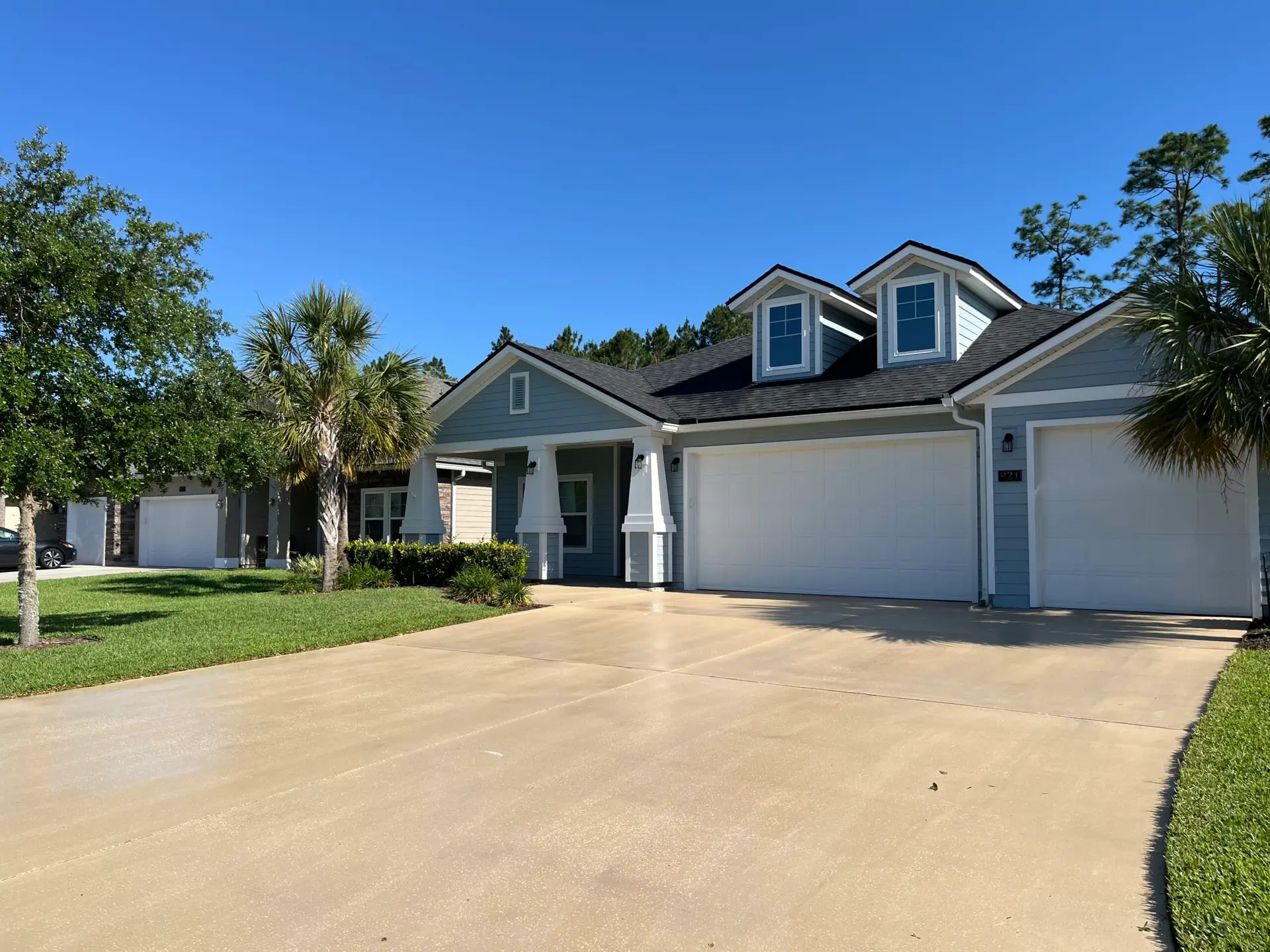 Clean concrete driveway leading to a white garage door on a blue-gray single-story home after concrete cleaning